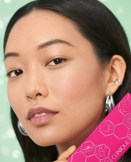 Portrait of an Asian female model promoting Clinique makeup, highlighting her flawless skin, silver earrings, and the cosmetic product.