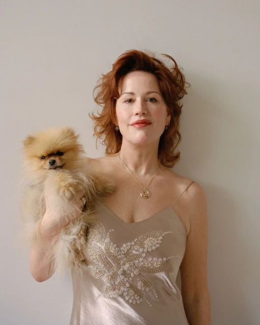 Woman in champagne dress poses with fluffy Pomeranian dog in a portrait with a neutral background.