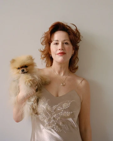 Woman in champagne dress poses with fluffy Pomeranian dog in a portrait with a neutral background.
