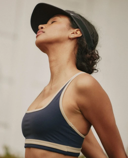 Athletic woman in a sports bra and visor outside with neutral background. Healthy lifestyle and fitness concept.
