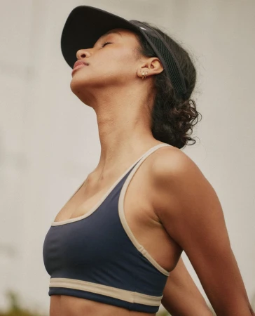 Athletic woman in a sports bra and visor outside with neutral background. Healthy lifestyle and fitness concept.