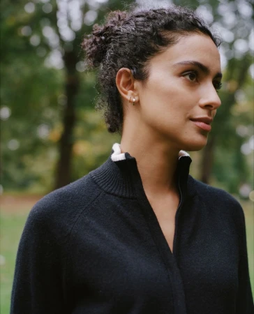 Portrait of a woman with dark curly hair wearing a black zip-up sweater in a park setting by photographer Katie Mccurdy.