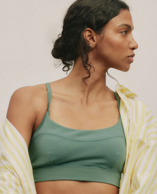 Portrait of a woman in a green sports bra and yellow striped shirt, looking off to the side, with a neutral studio background.