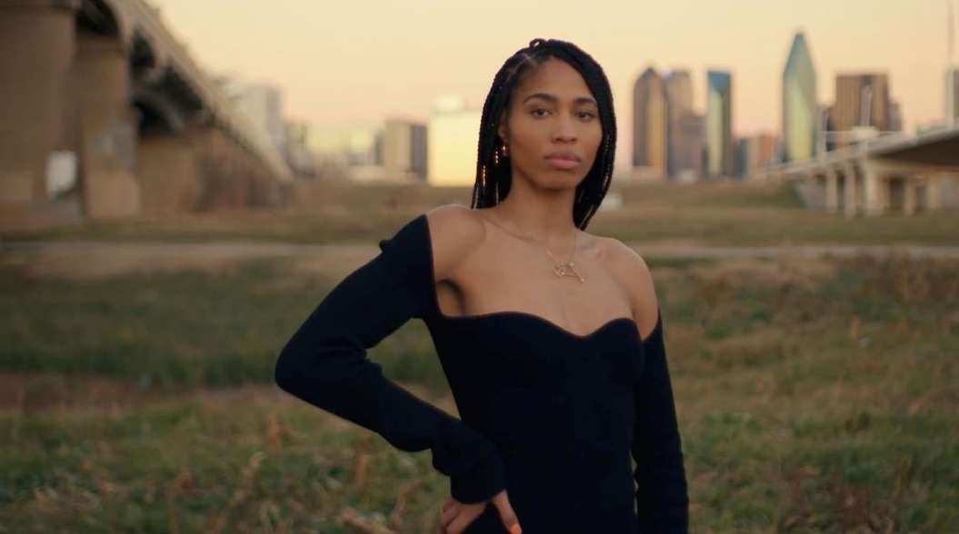 Woman in stylish dress poses outdoors with city skyline. Fashion shot captures modern elegance in urban setting, with natural light.