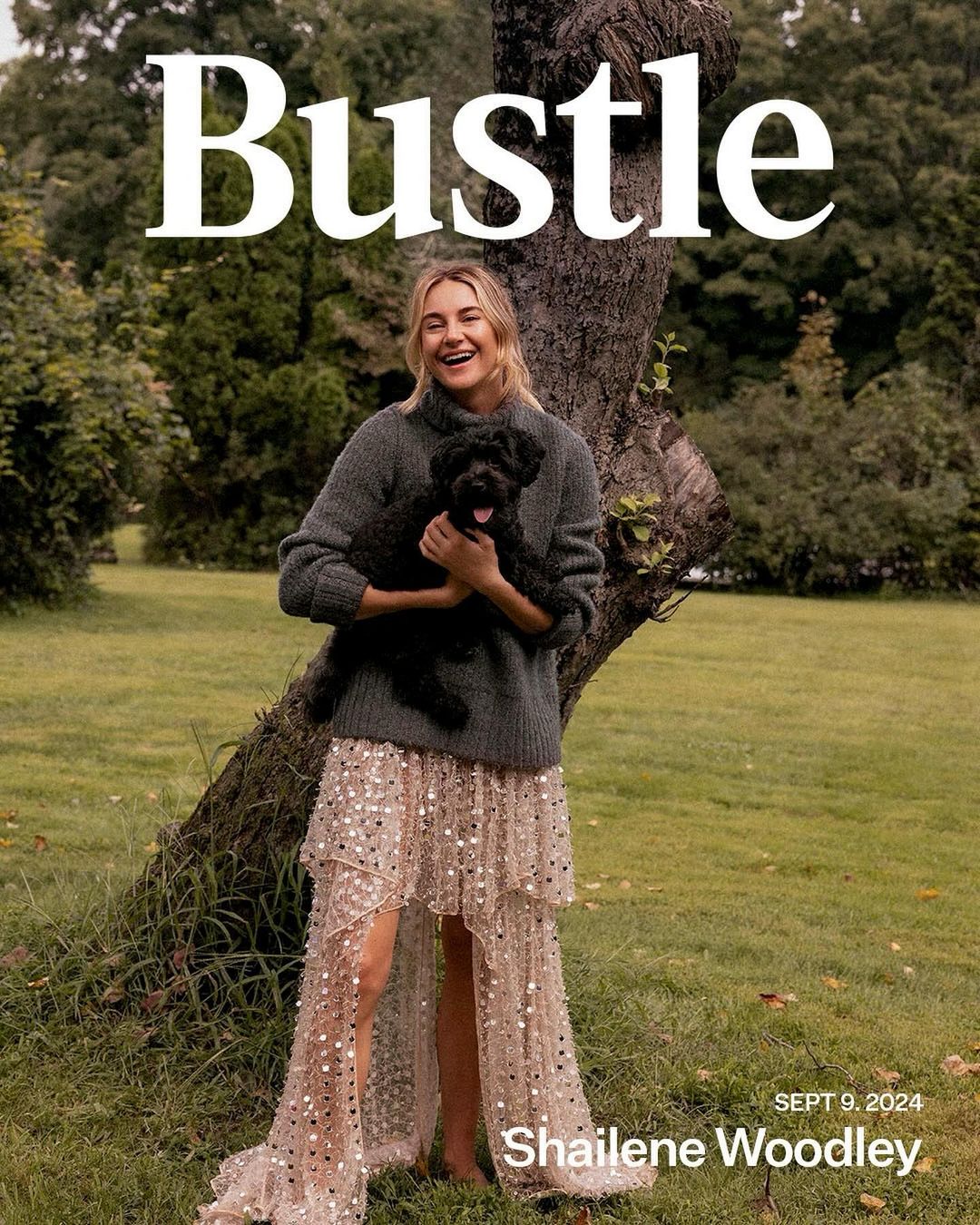 Shailene Woodley on the cover of Bustle magazine with a dog. She wears a grey sweater and a long dress in an outdoor environment.