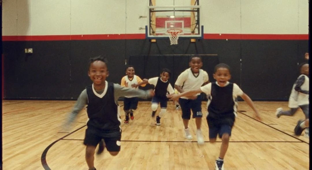 Group of African American children running on a basketball court, smiling with joy. Indoor sports hall setting with a basketball hoop.