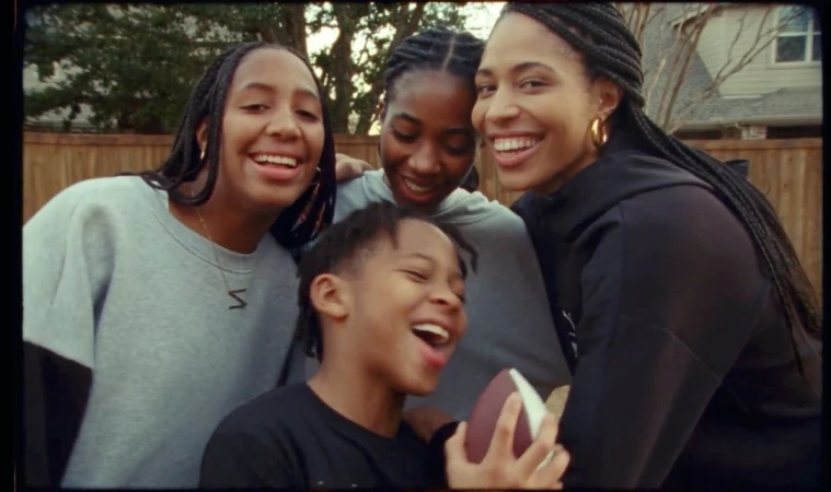 Outdoor family group portrait features four smiling African-American people, including a young boy with a football, in a backyard.