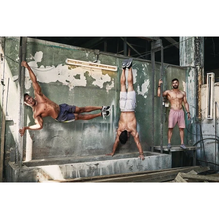 Three muscular men demonstrate advanced calisthenics poses against a weathered concrete wall in an industrial-style setting.