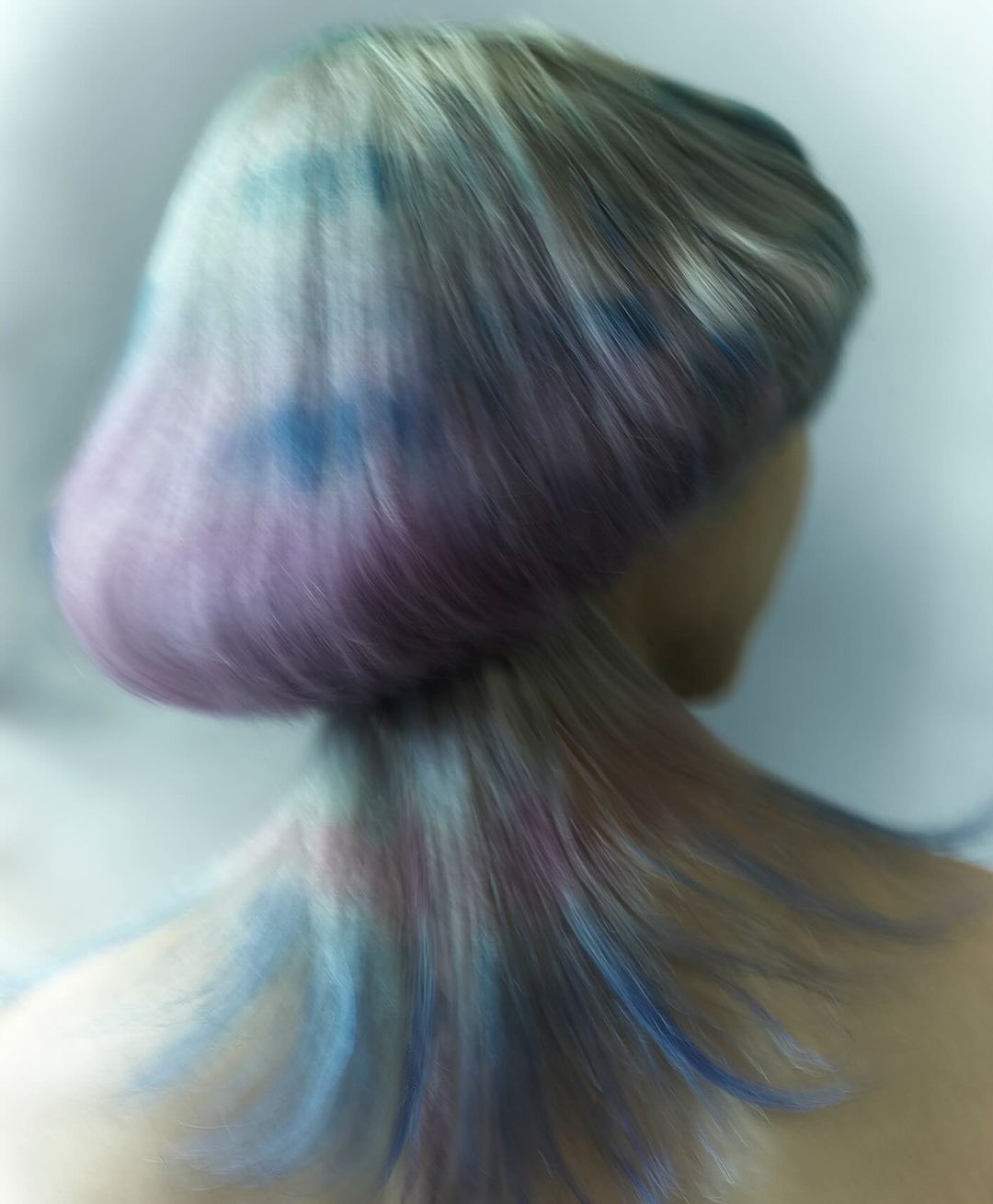 Close-up rear view of a person with short, layered hair dyed in pastel shades of blue, purple, and gray against a blurred light background.