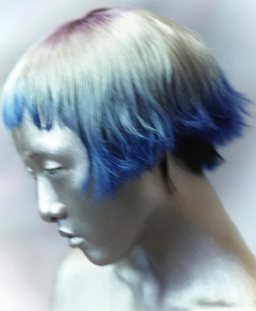 Asian woman with striking silver body paint and vibrant blue hair, her gaze lowered, creating a captivating and surreal visual aesthetic.
