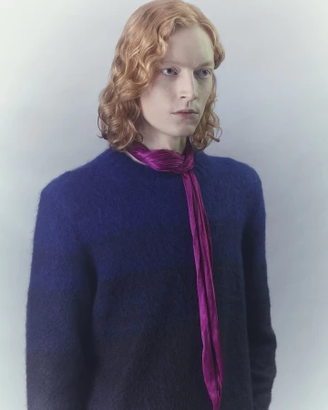 Portrait of a redhead adult male wearing a blue ombre sweater and a magenta scarf, set against a solid grey studio background.