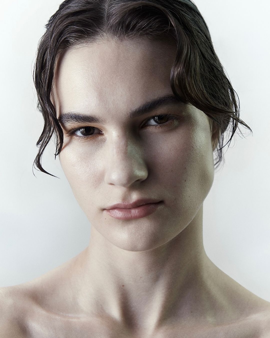 Close-up portrait of a young woman with dark hair and wet strands framing her face against a plain white background.