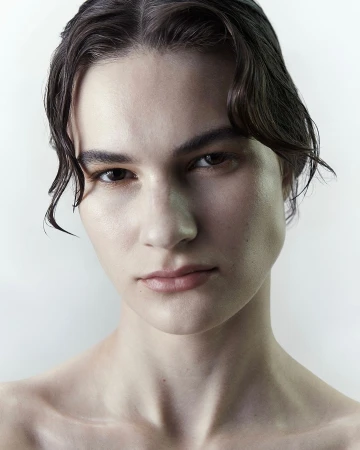 Close-up portrait of a young woman with dark hair and wet strands framing her face against a plain white background.