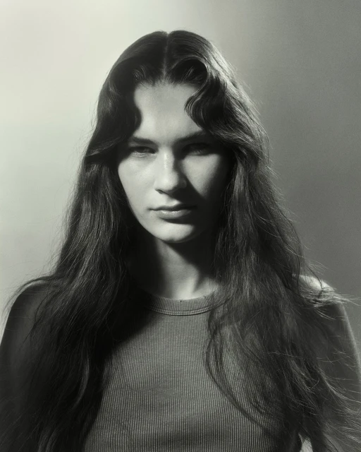Monochrome portrait of a young woman with long wavy hair, wearing a ribbed crew-neck top, against a softly lit gradient backdrop.