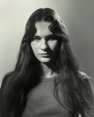 Monochrome portrait of a young woman with long wavy hair, wearing a ribbed crew-neck top, against a softly lit gradient backdrop.