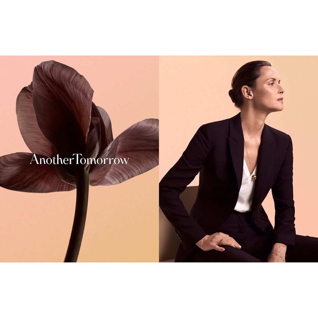 Woman in a black suit is posing next to a flower, split by a beige background with the text 'Another Tomorrow'.