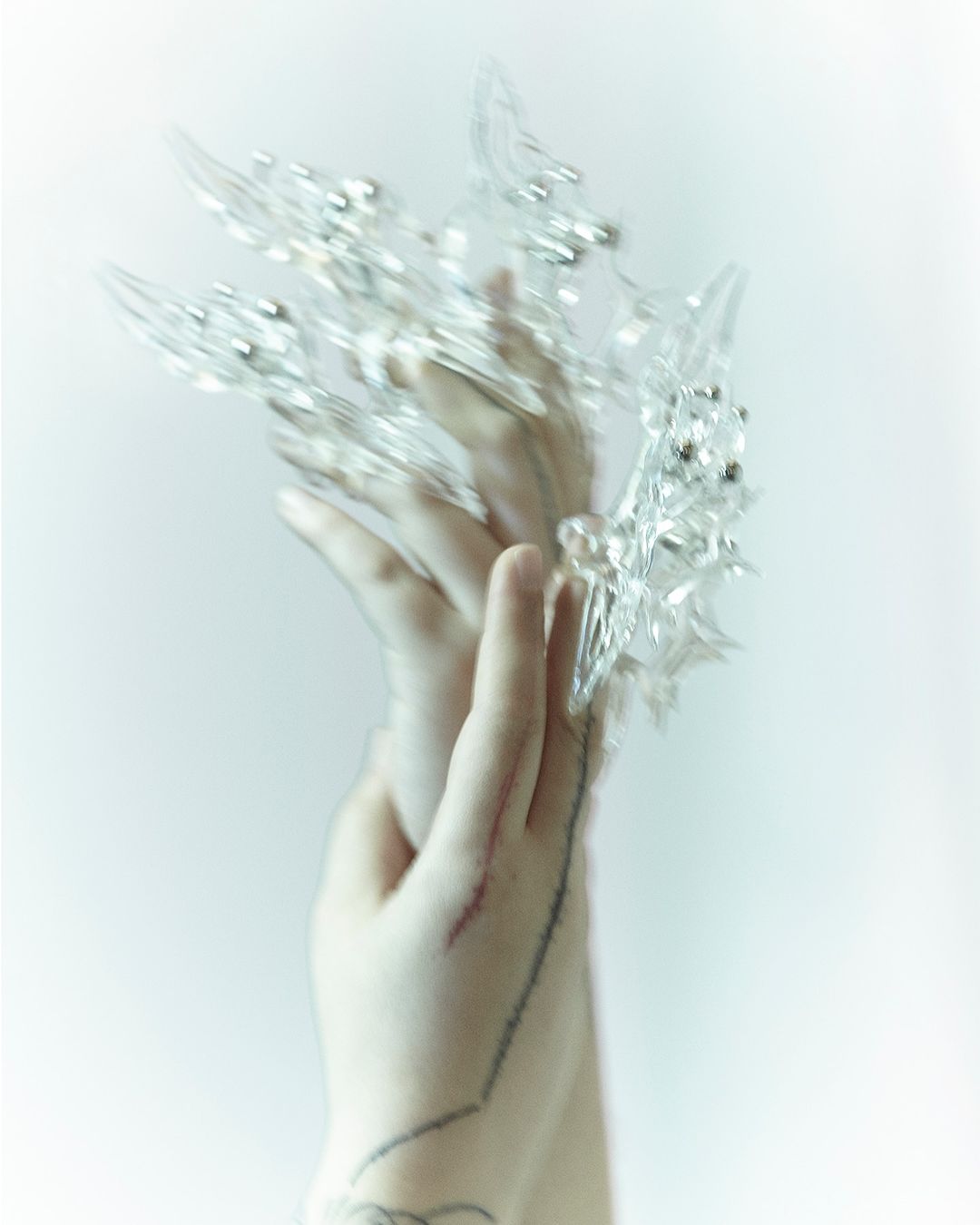 Woman's hands with clear crystal claw jewelry over the fingers, set against a plain light background. Beauty and fashion accessory.