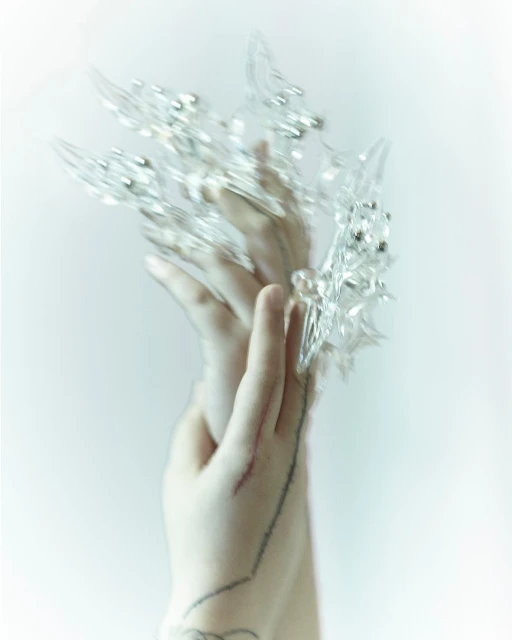 Woman's hands with clear crystal claw jewelry over the fingers, set against a plain light background. Beauty and fashion accessory.