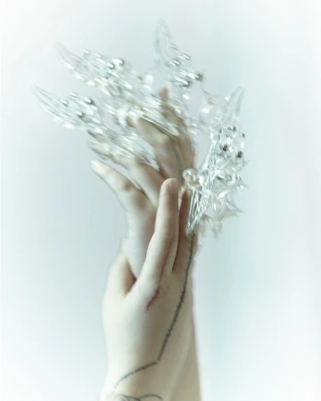 Woman's hands with clear crystal claw jewelry over the fingers, set against a plain light background. Beauty and fashion accessory.