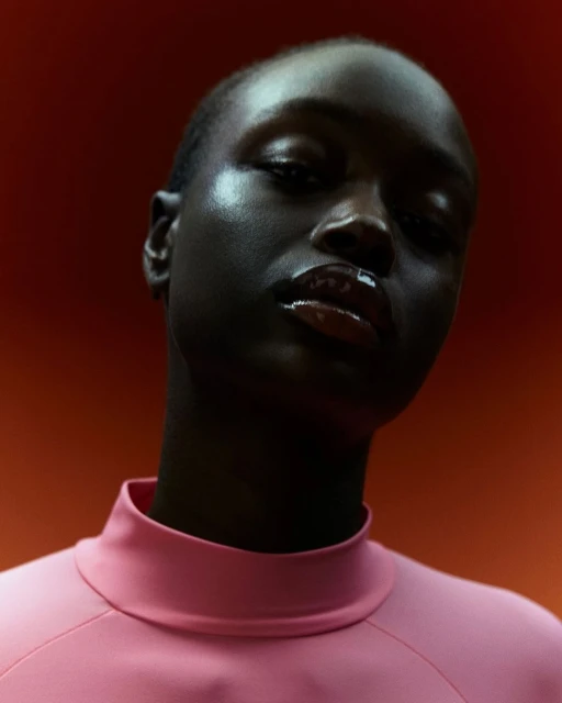 Close-up studio portrait of a Black female model in pink top against a warm orange background, showcasing beauty and fashion aesthetics.