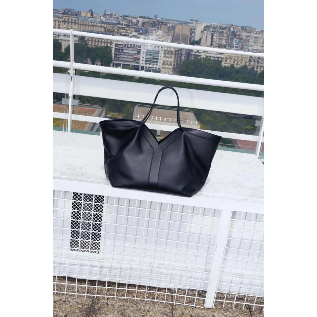 Elegant black leather tote bag with long handles on a white lattice table against an urban cityscape backdrop, minimalist fashion.