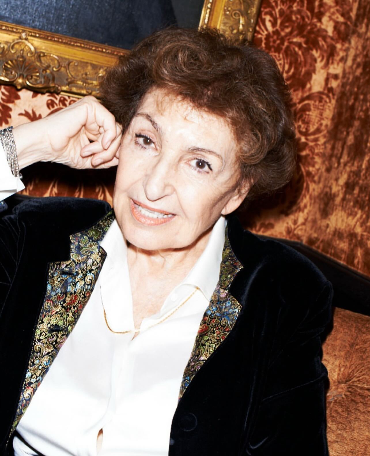 Portrait of an elderly woman with curly auburn hair, wearing a black velvet jacket and white blouse, with an ornate gold frame in the background.