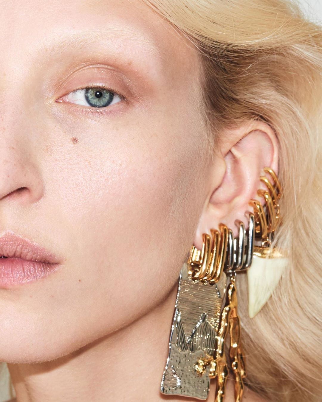 Close-up of a fair-skinned adult woman with pale blonde hair wearing gold and silver statement jewelry, showcasing fashion beauty.