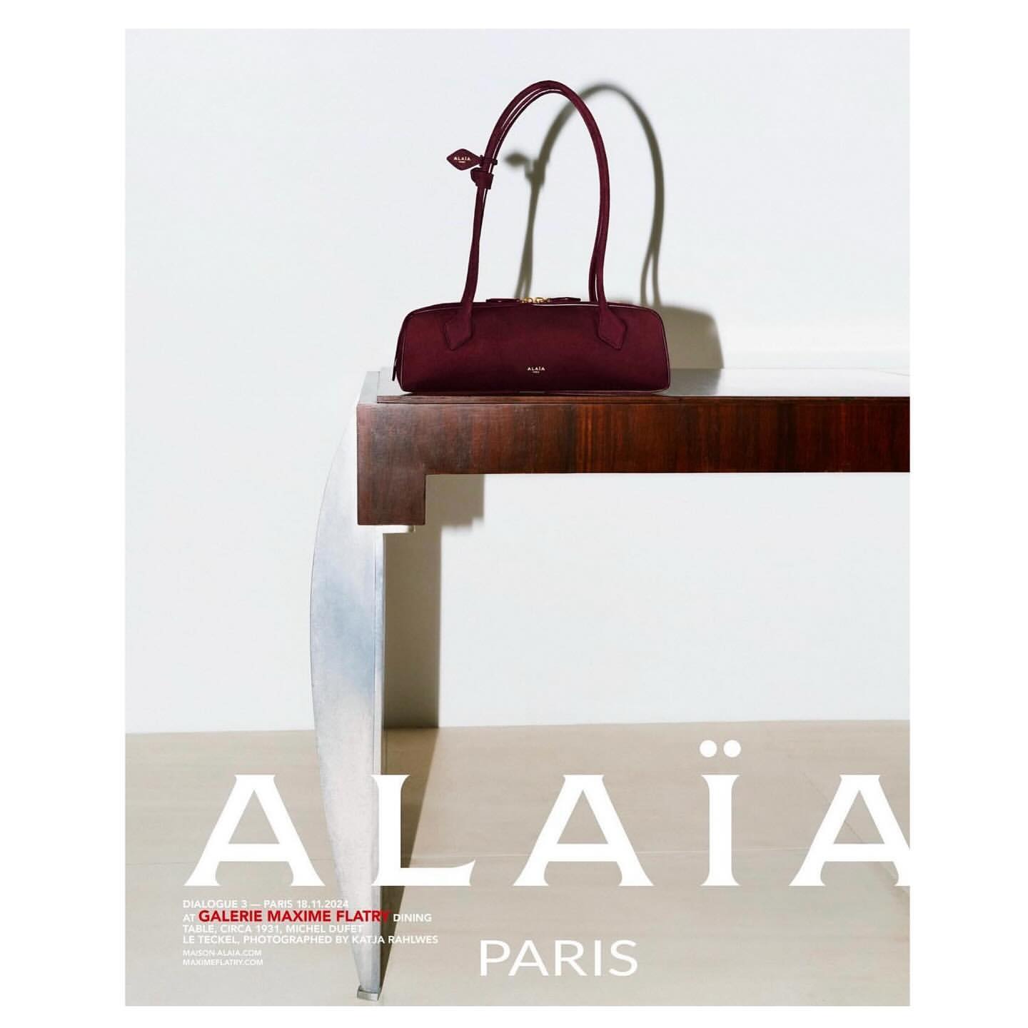 Alaïa burgundy purse is displayed on a dark wood table in a fashion editorial ad against a white backdrop with brand logo.