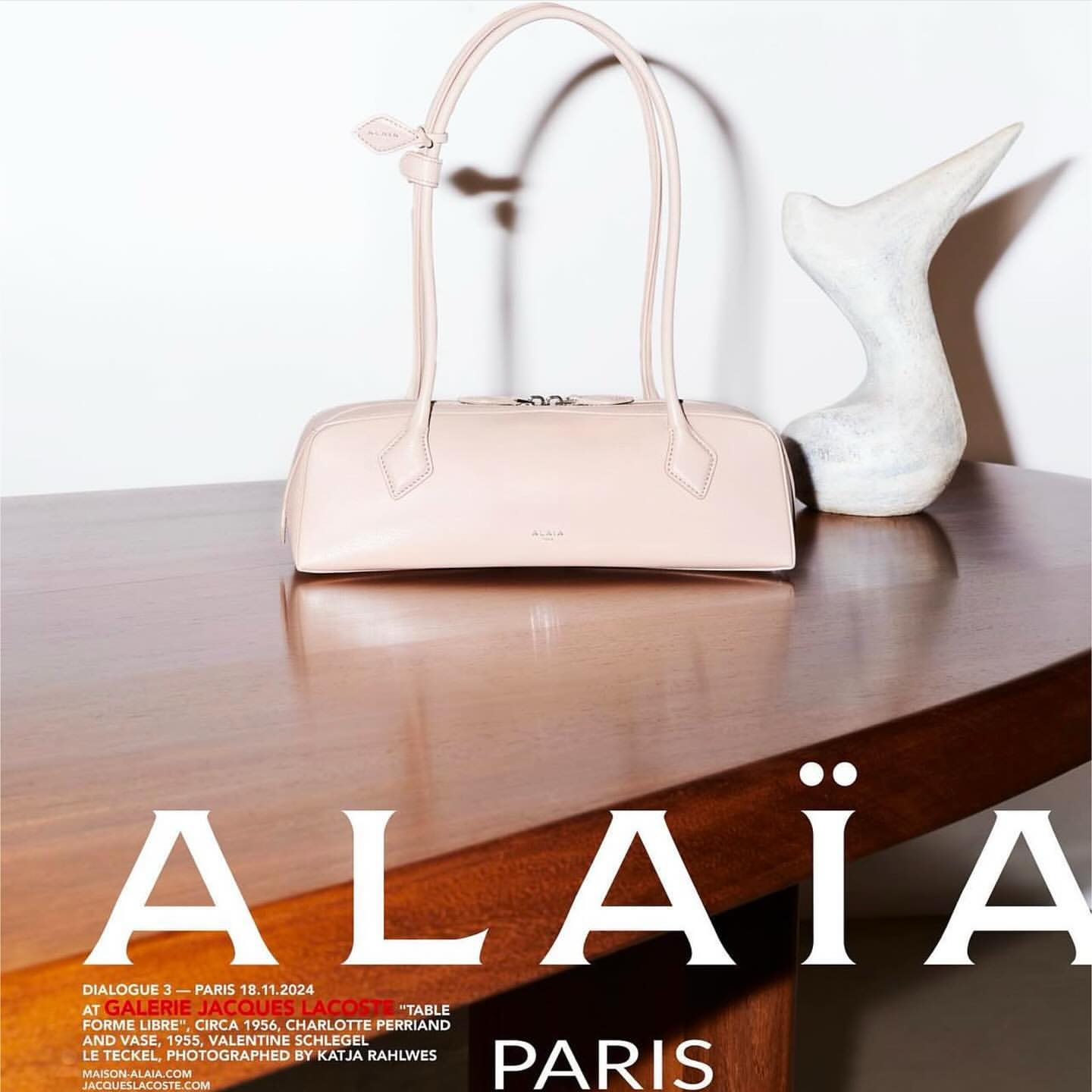 Elegant cream-colored leather handbag with dual top handles on a polished wood table, paired with a modern white sculpture.