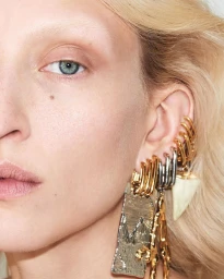 Extreme close-up portrait of a woman wearing multiple stacked gold and silver earrings and a large pendant.