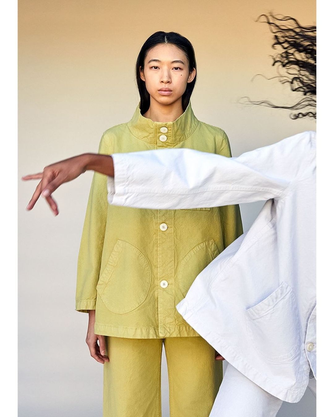 Portrait of an East Asian woman wearing a chartreuse buttoned jacket standing beside a person in white