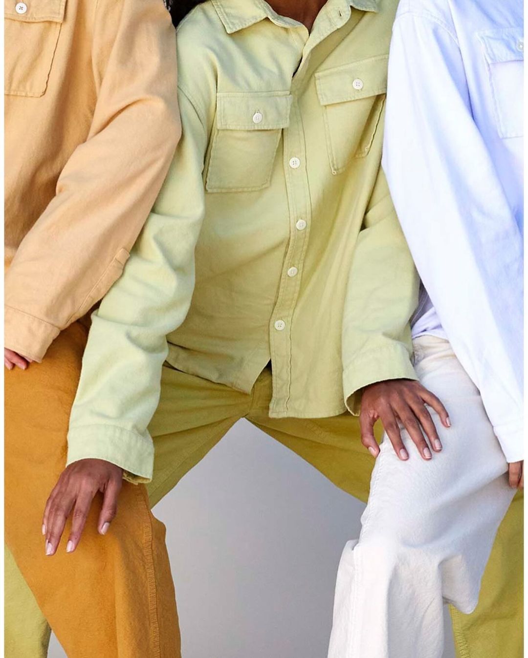 Three people wearing yellow, green, and white button-down shirts with matching pants, hands visible, and posing against a plain background.