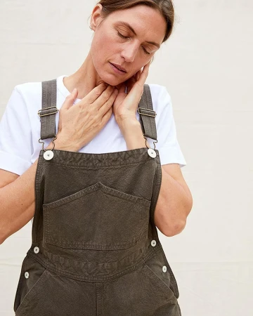 Woman wearing grey overalls over a white t-shirt against a plain white background by photographer Katrina Dickson