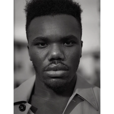 Portrait of a young adult Black man in a collared shirt, looking directly at the camera in a close-up, monochrome studio shot.