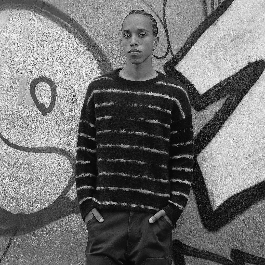 Portrait of a man with cornrows wearing a striped sweater against a graffiti wall by Katsu Naito