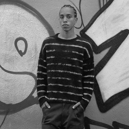 Portrait of a man with cornrows wearing a striped sweater against a graffiti wall by Katsu Naito
