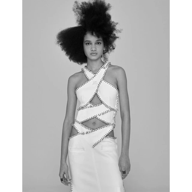 Black and white portrait of a woman with afro hairstyle wearing a sleeveless top and skirt with cutouts against a grey background.