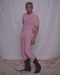 Asian man wearing a textured pink polo shirt and trousers paired with dark boots against a draped backdrop