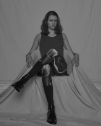 Portrait of a person seated with legs crossed in a draped chair wearing patterned leggings and boots