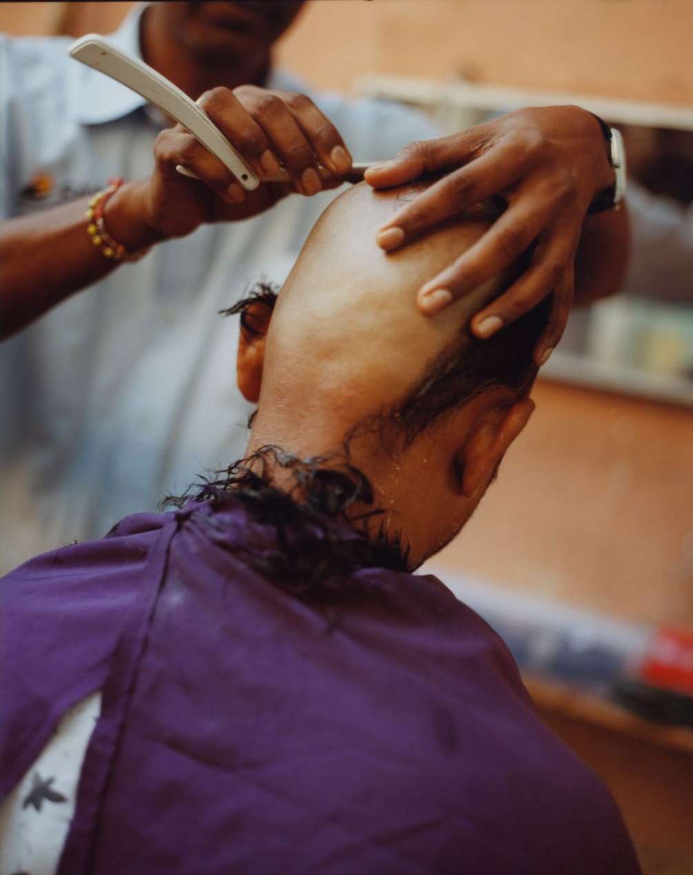 Close-up of a man receiving a head shave with a straight razor from a barber, focusing on the razor and the bald head.