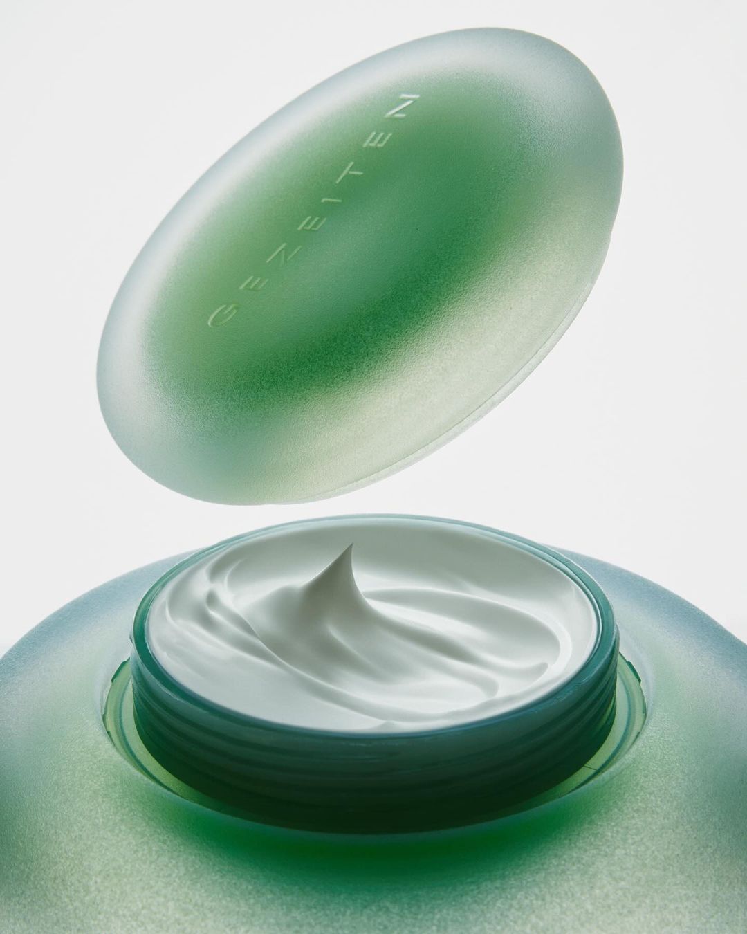 Close-up of a frosted green jar of moisturizing cream with a separate lid, product shot for skincare or beauty advertising.