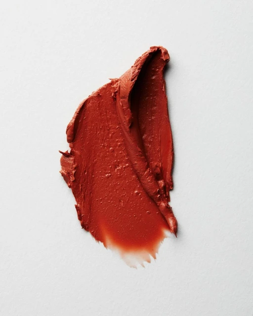 Textured smear of vibrant red lipstick on a clean, light background. Cosmetic product shot for beauty or makeup advertising.