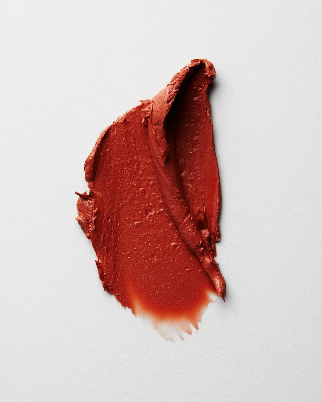 Macro shot of a smear of vibrant red-orange lipstick against a plain white backdrop, showcasing its rich texture and color.