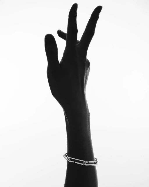 Close-up studio shot of an arm with a silver chain-link bracelet in a high-key, black-and-white image. The hand is raised with fingers extended.