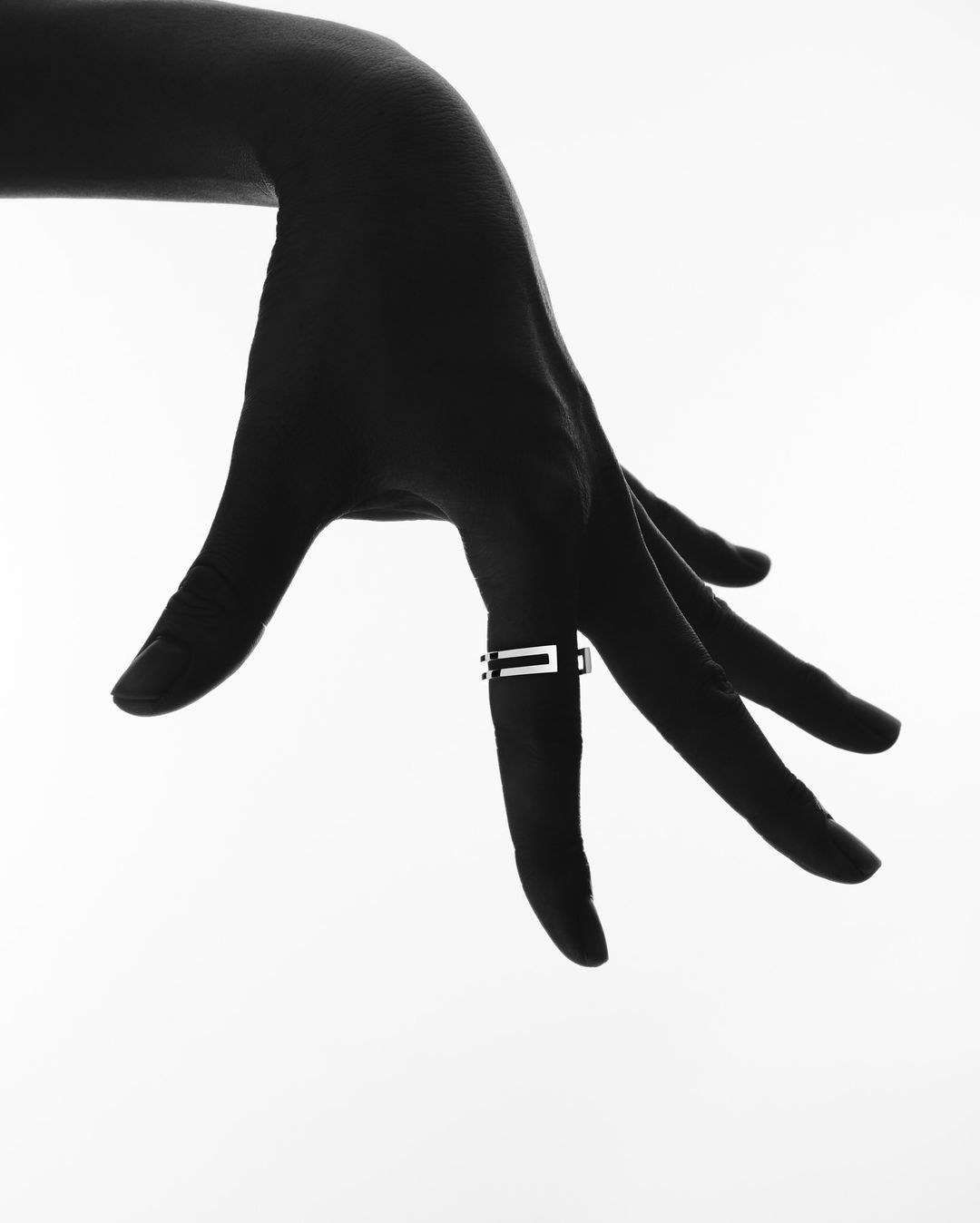Close-up studio shot of an adult female's hand with a ring on the middle finger against a solid white background. Black and white.