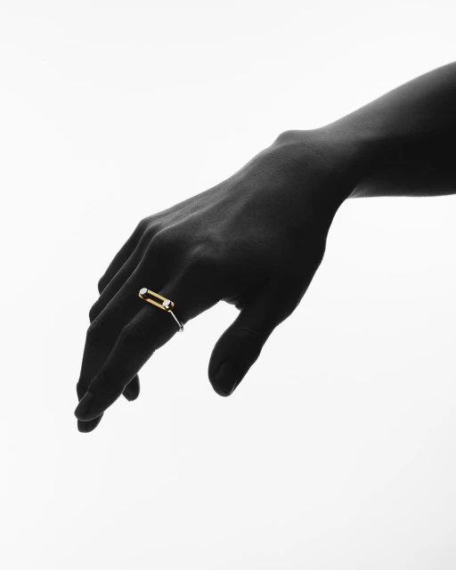 Close-up of a dark-skinned hand wearing a modern ring with a gold band and white gemstone detail against a stark white background.