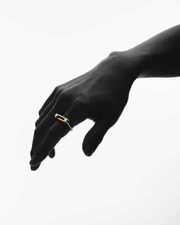 Close-up of a dark-skinned hand wearing a modern ring with a gold band and white gemstone detail against a stark white background.