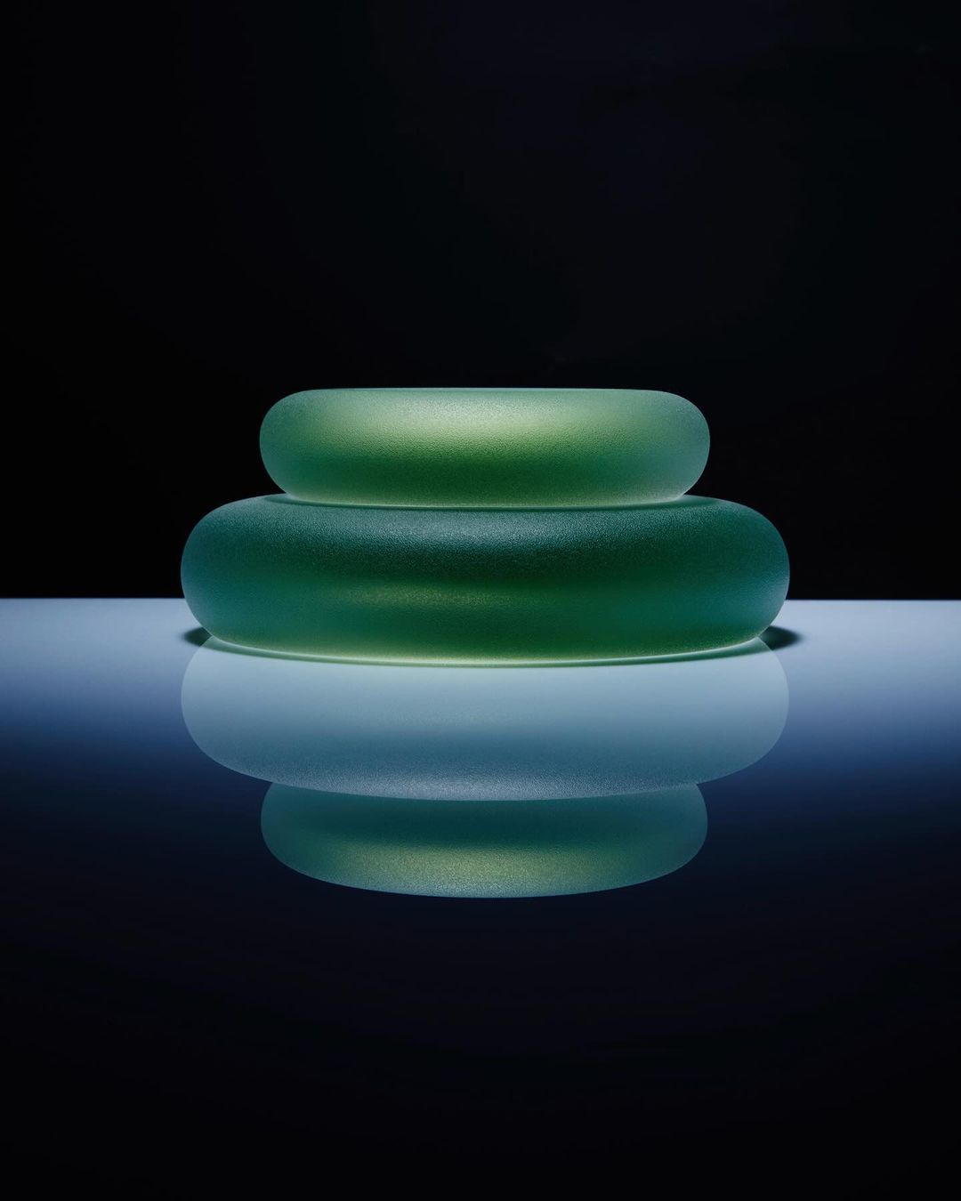 Green glass bangles stacked on a reflective surface against a dark background in a studio shot with soft lighting. Product shot.