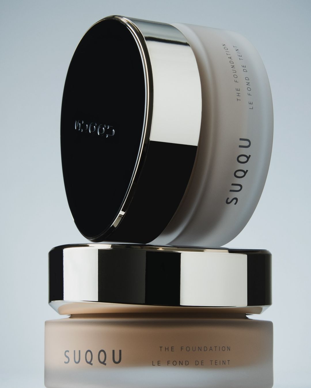 Stacked SUQQU foundation jars show their elegant packaging and varying shades against a muted background, enhancing brand visibility.