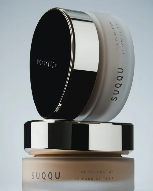Stacked SUQQU foundation jars show their elegant packaging and varying shades against a muted background, enhancing brand visibility.